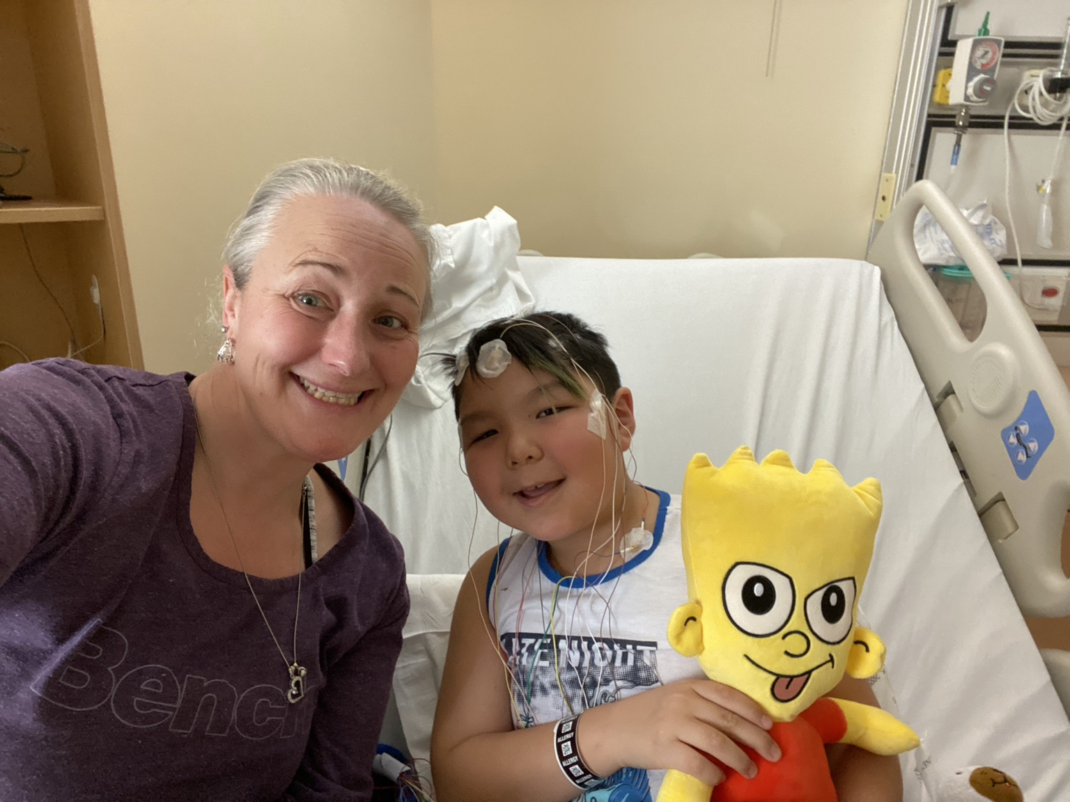 Lucas with his mom Kathy during a sleep study, smiling together while Lucas is connected to monitoring sensors